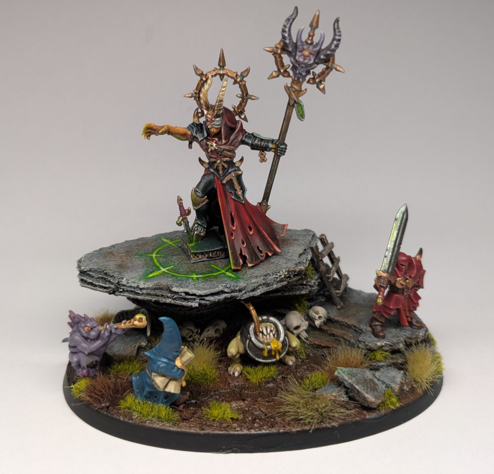 A painted Warhammer miniature with a chaos sorcerer standing on a rock surrounded by nefarious minions