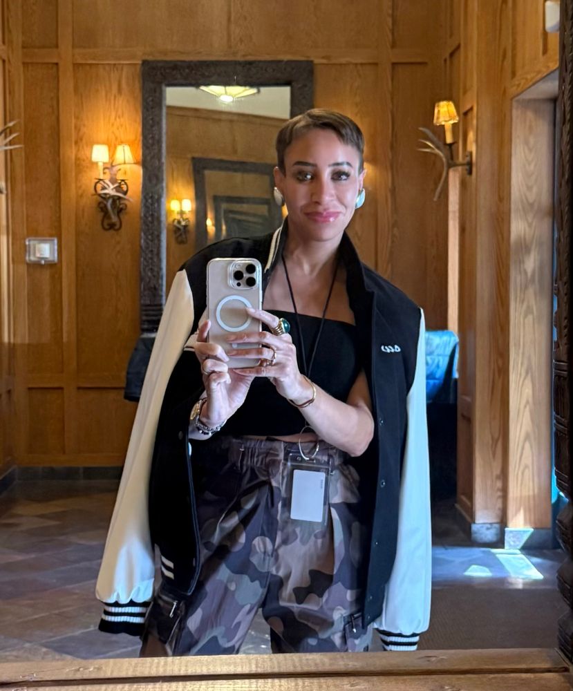 Mirror selfie in wood-paneled foyer: camo pants, black tube top, black and white varsity jacket, vibes