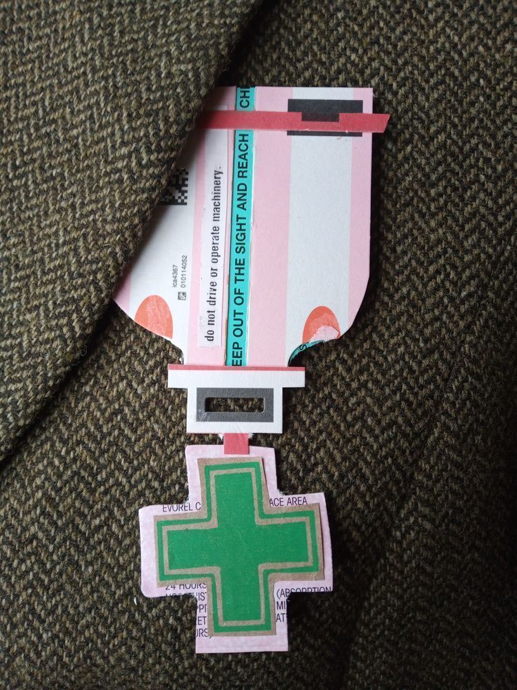 A hand-made medal pinned to a tweed jacket.  The medal is made from prescription packaging.