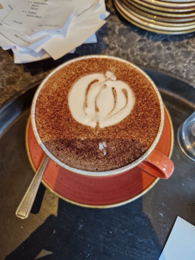 A chai latte with cinnamon on top, with latte art depicting a pumpkin. Halloween style