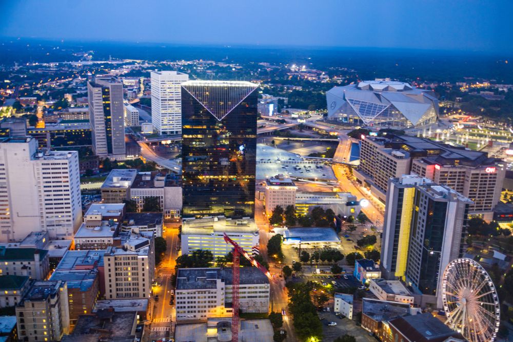 Cityscape at night: a view above many buildings and a ferris wheel.