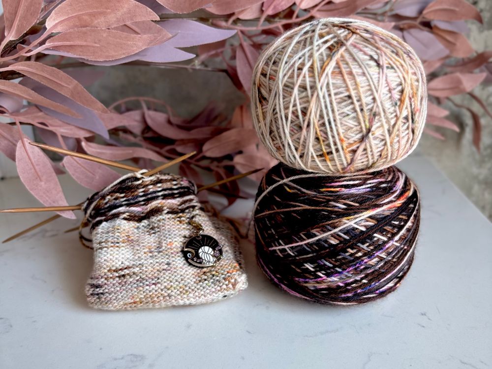 A partially knit colourwork sock sits on a countertop next to two cakes of matching yarn. 