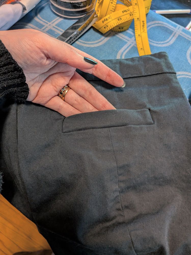 A close-up photo of a hand showing off the back of a pair of shorts. A welt pocket has been set into the shorts.