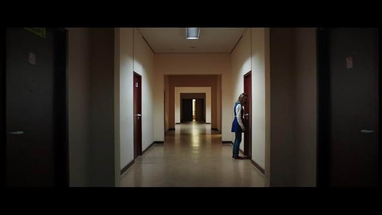 Interior of the university dorms, dimly lit. Justine stands at the door of her room. The space is immaculate, but it won't be for long.