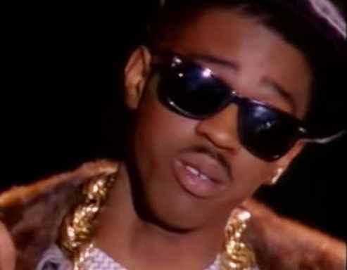 Bust of a young Slick Rick with blacksunglasses, a gold rope chain, and a fur coat.