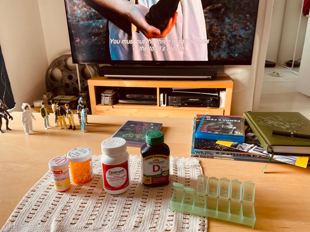 Pills being readied to be placed in a daily pill organizer; Pan’s Labyrinth is on the TV beyond