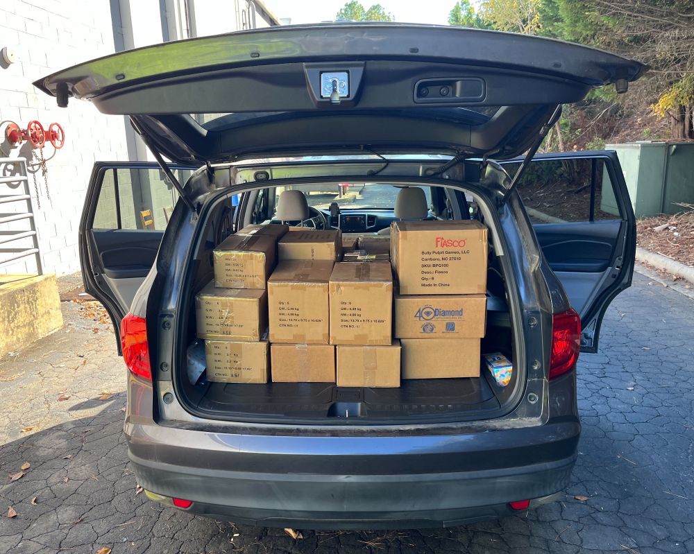 A grey SUV is shown with all of its doors opened. The second row of passenger seats are folded down and the interior cabin space is nearly packed full with the boxes from the other photograph!