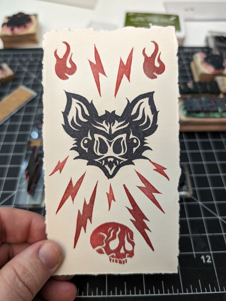Photo of a hand holding a hand printed bookmark of a black bat with red radiating lightning bolts