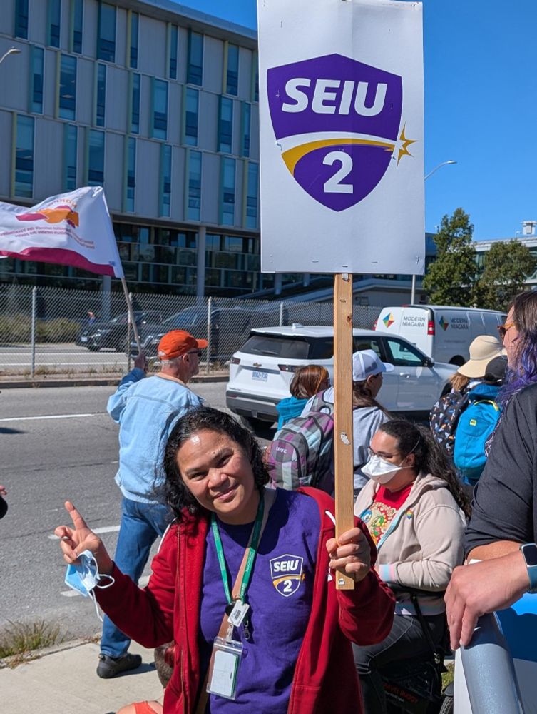 Member Cherry on the picket line in solidarity holding a peace sign and SEIU Local 2 sign. 