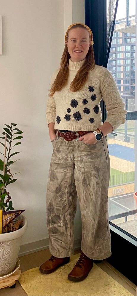 Full-body picture of the same woman. She is also wearing irregularly bleached grey jeans and brown combat boots. 