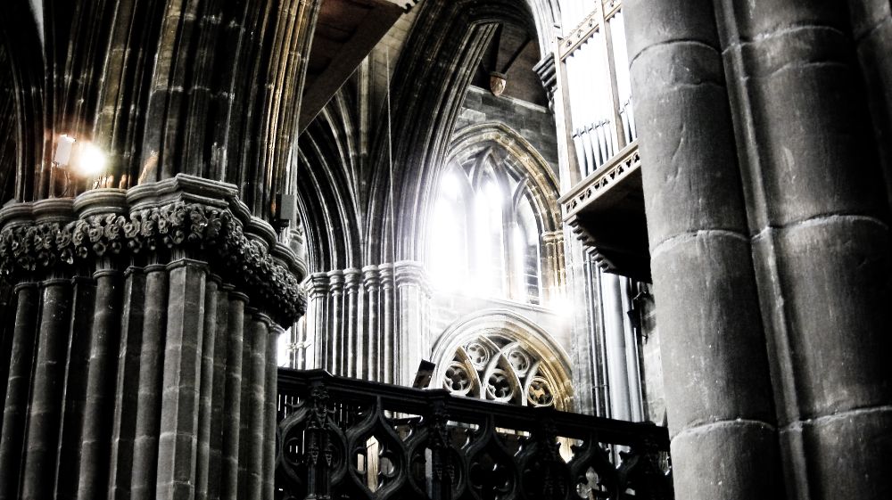 A stunning view of the intricate Gothic architecture inside a cathedral in Glasgow, with light streaming through the windows and illuminating the stone columns.