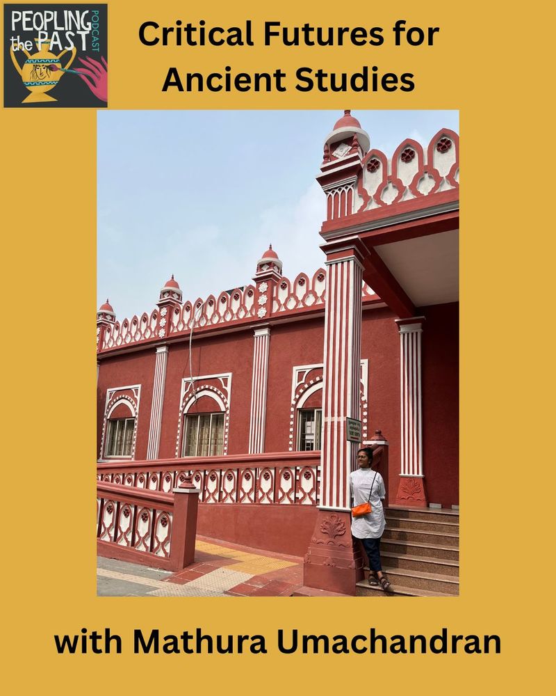 Mathura stands at the foot of a set of steps leading up to the porch of an imposing building behind her. The building is a mix of architectural styles, with columns and porch adorning the set of stairs. The brick appears to be painted in an orange-brown colour, with white details.