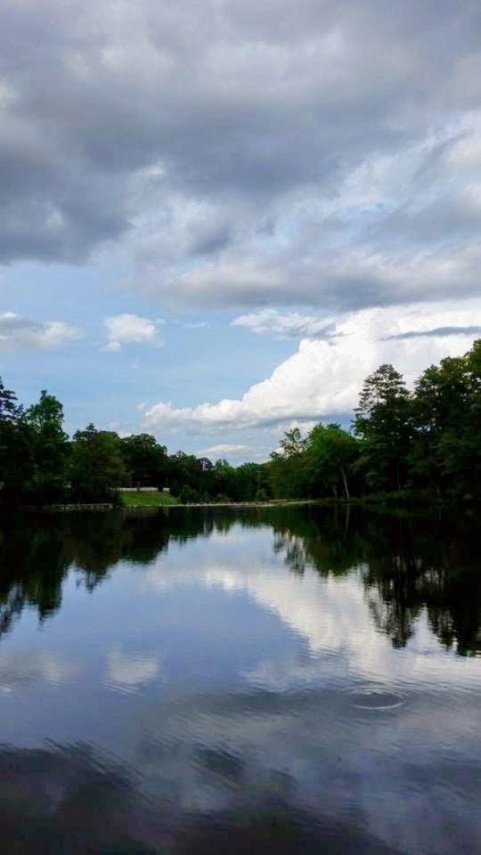 I'm not sure where I am here, but this is a nice photograph of a lake with blue sky with white and grey puffy clouds reflecting off the water from my camera roll. Taken in 2020.