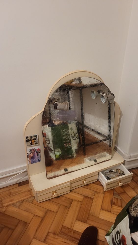 Penteadeira cor marfim, arredondada e com três gavetas (sem pés pois é suspensa mas na foto aparece no chão) com espelho arredondado de base reta com duas lampadas integradas, estilo "bastidor"