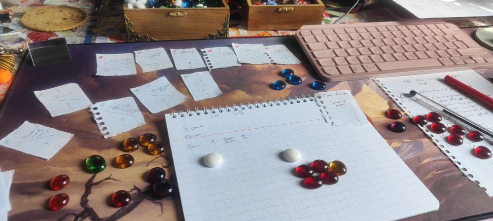 A desk covered in small torn papers and glass beads. The papers look like simplified playing cards with attacks and skills written on them.