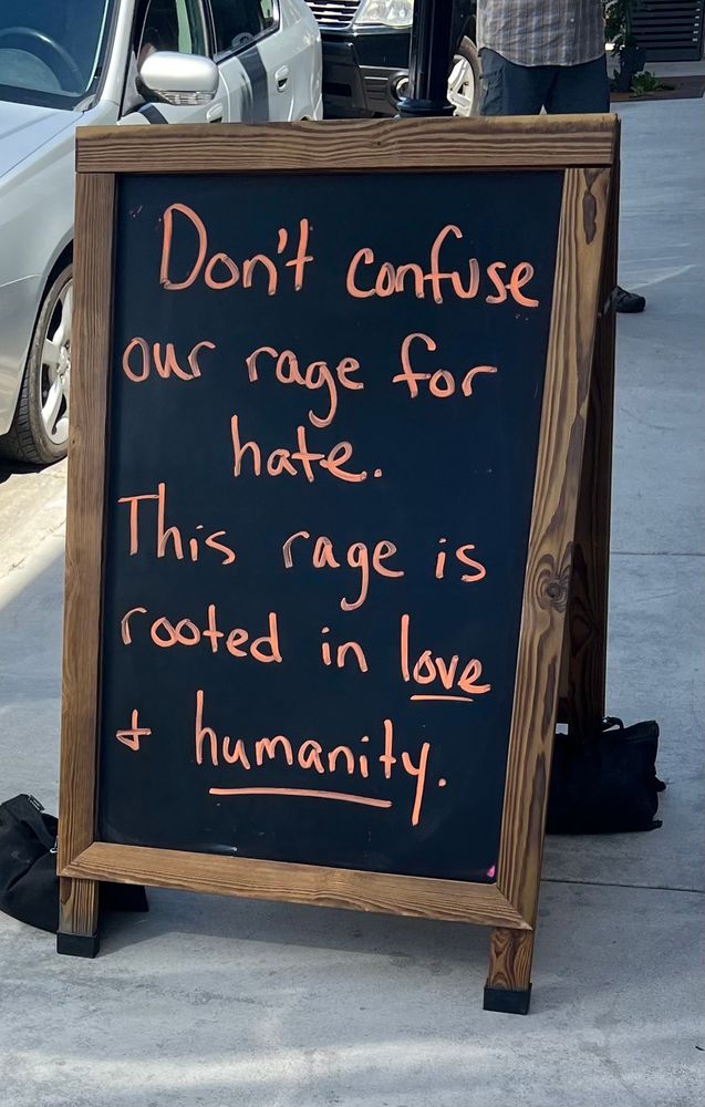 Chalk signboard on the street.  Written in orange:
“Don’t confuse our rage for hate.
This rage is rooted in love and humanity.”

(Love and humanity are underlined)