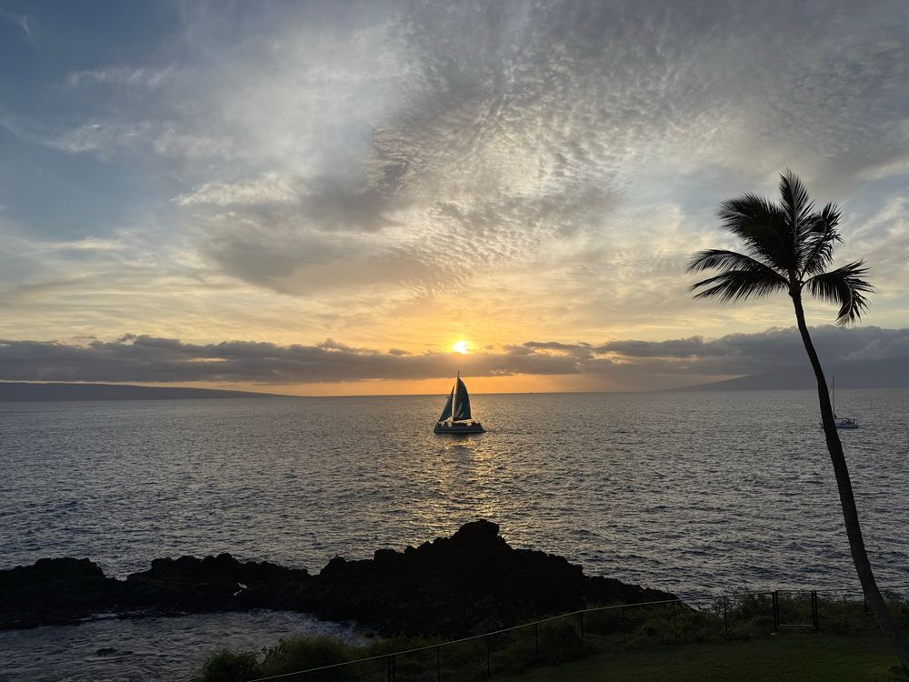 Sailboat in the ocean with the sunset behind it.