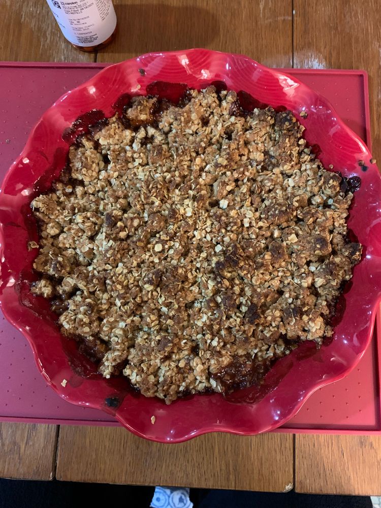 Toasted golden oats and crispy topping display from a Birds Eye view. brown syrupy stains line the crisp from the bubbling of the apple filling when it was cooking. Baked in a wavy red pie plate. 