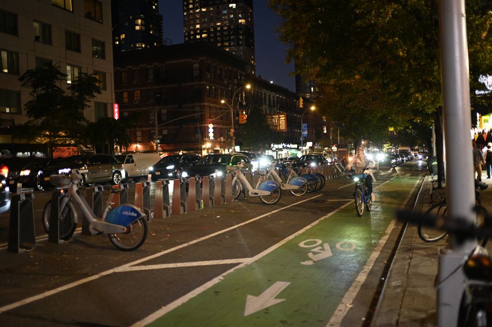 A woman riding past on a Citi bike in a bike lane with a dock that looks like it has 30 stalls or so