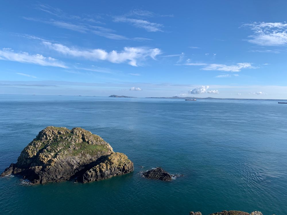 A photo of the Garland Stone, a large rock off the north coast of Skomer. The sea and sky are very blue and the sea is calm.