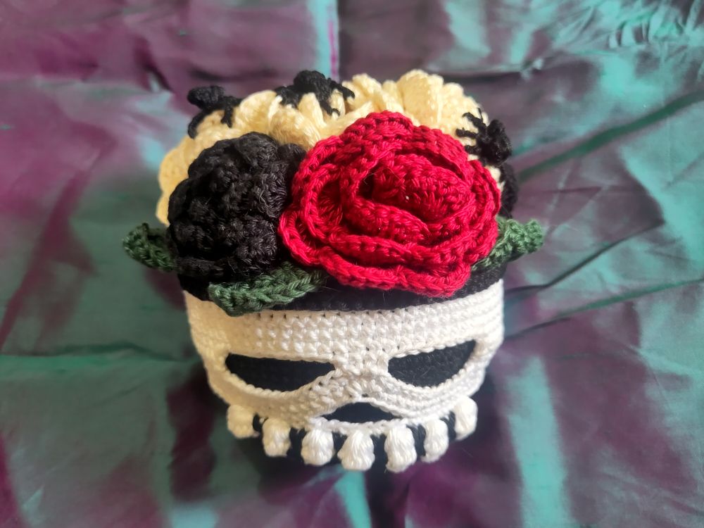 Crochet skull with red, black and cream roses on top. The cream roses have spiders on them.