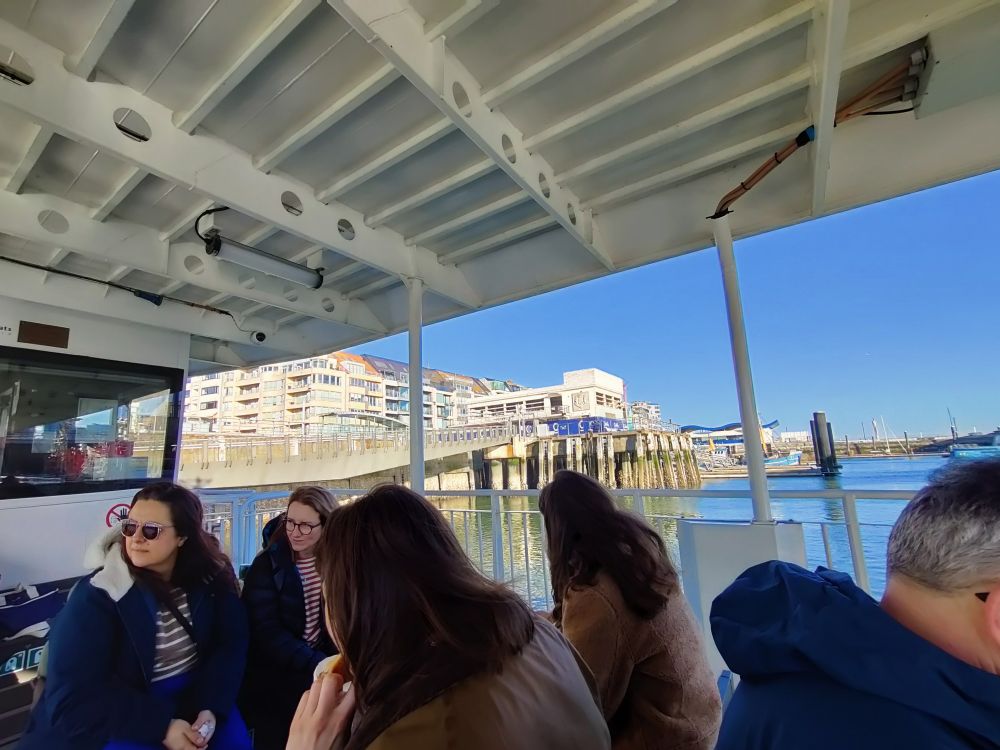 Picture of 4 women sitting on a small passenger ferry as it departs its mooring. Bright blue sky in the background