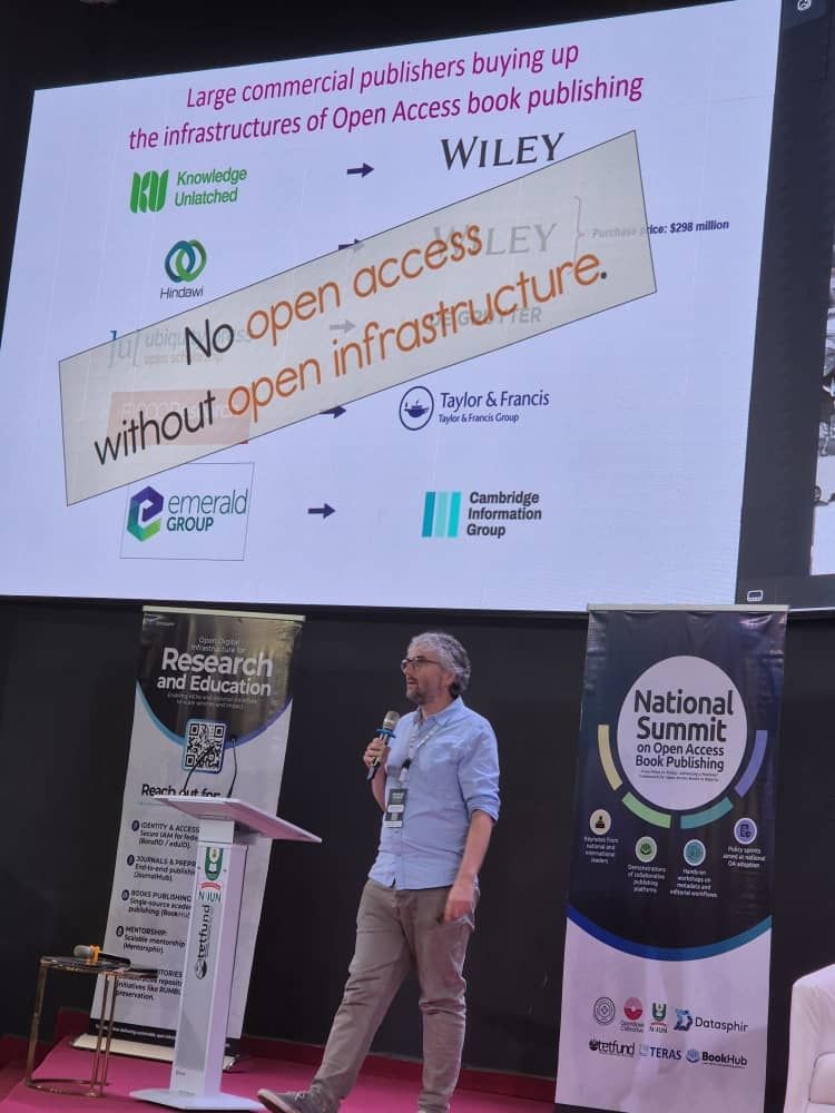 Joe Deville at a podium, in front of a slide with a banner reading 'No open access without open infrastructure'
