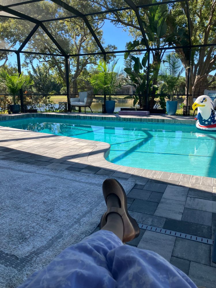 Sitting in a chair, looking at a small pool with an eagle floaty, some chairs, and some water in the distance