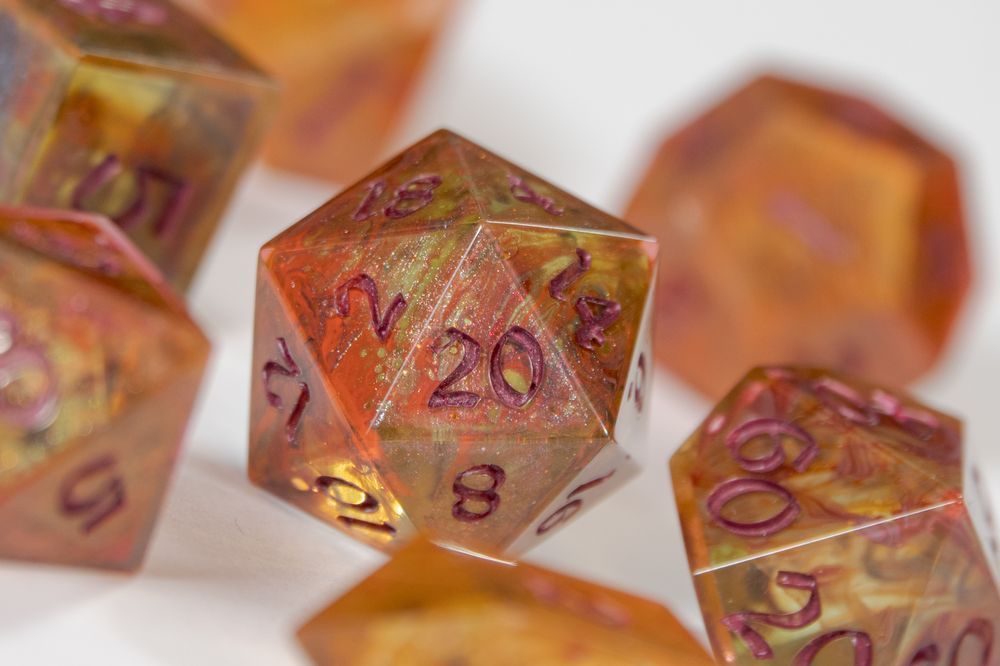 A set of dice in different red, yellow and orange colours on a white background. The d20 is in focus.