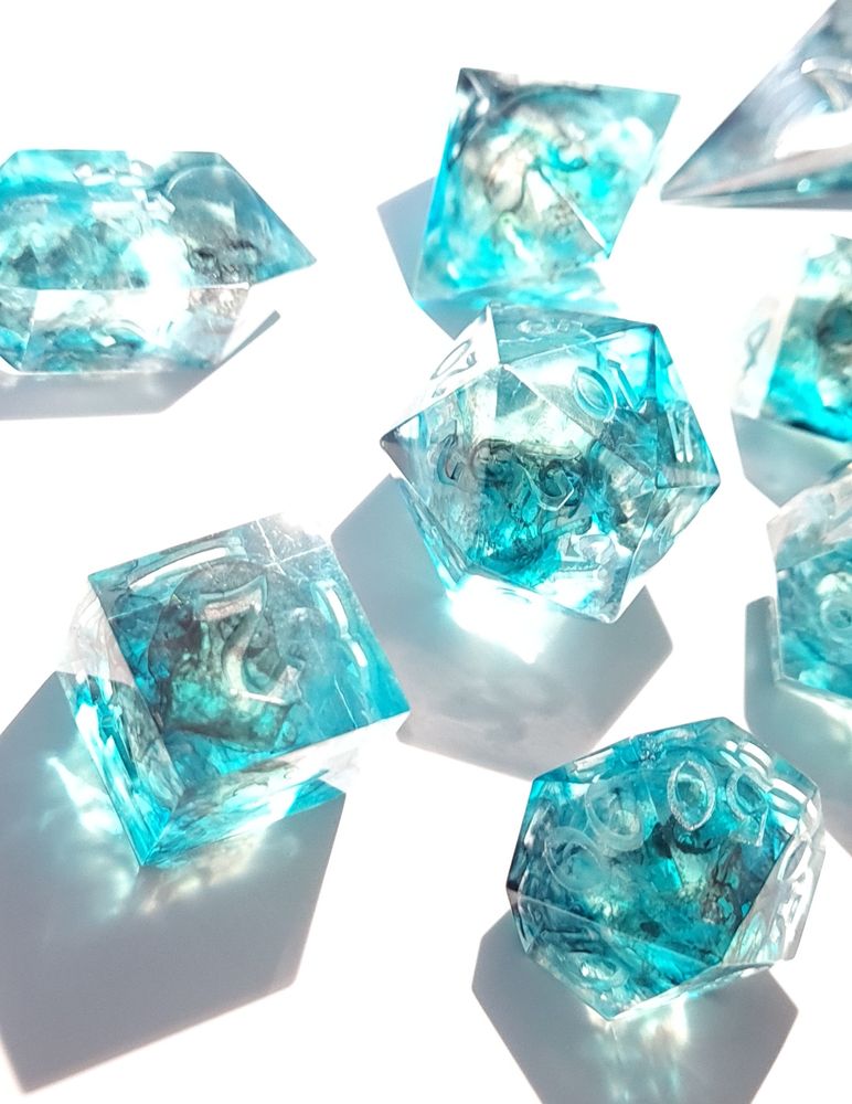 A set of light blue dice with very faint skulls inside them on a white background 