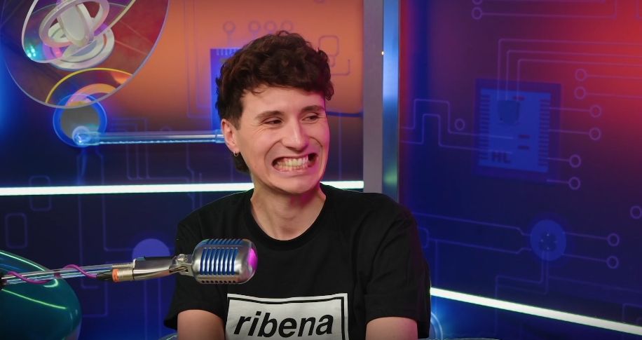 Dan Howrll in a black shirt that says "ribena" exposing all his teeth and staring emotionless lungs to the right