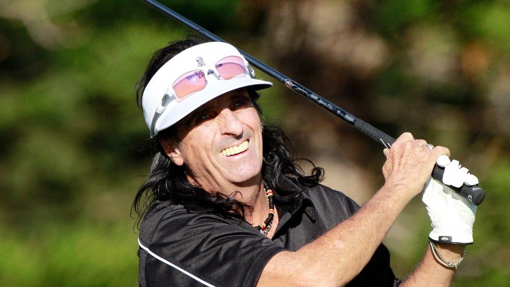 Picture showing a smiling Alice Cooper swinging a golf club on the course.