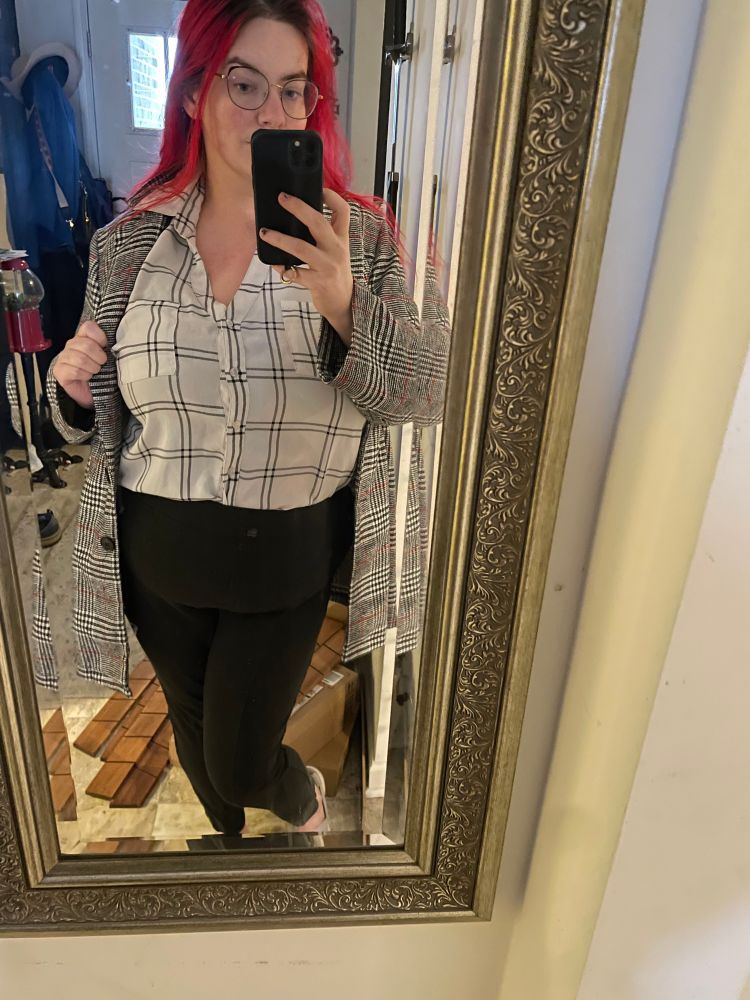I am wearing a white with black grid button up shirt tucked into a pair of charcoal, skinny leg trousers. Over it I am wearing a black, white and red plaid oversized blazer. The collar of the shirt is splayed out over the collar of the jacket for emphasis. 