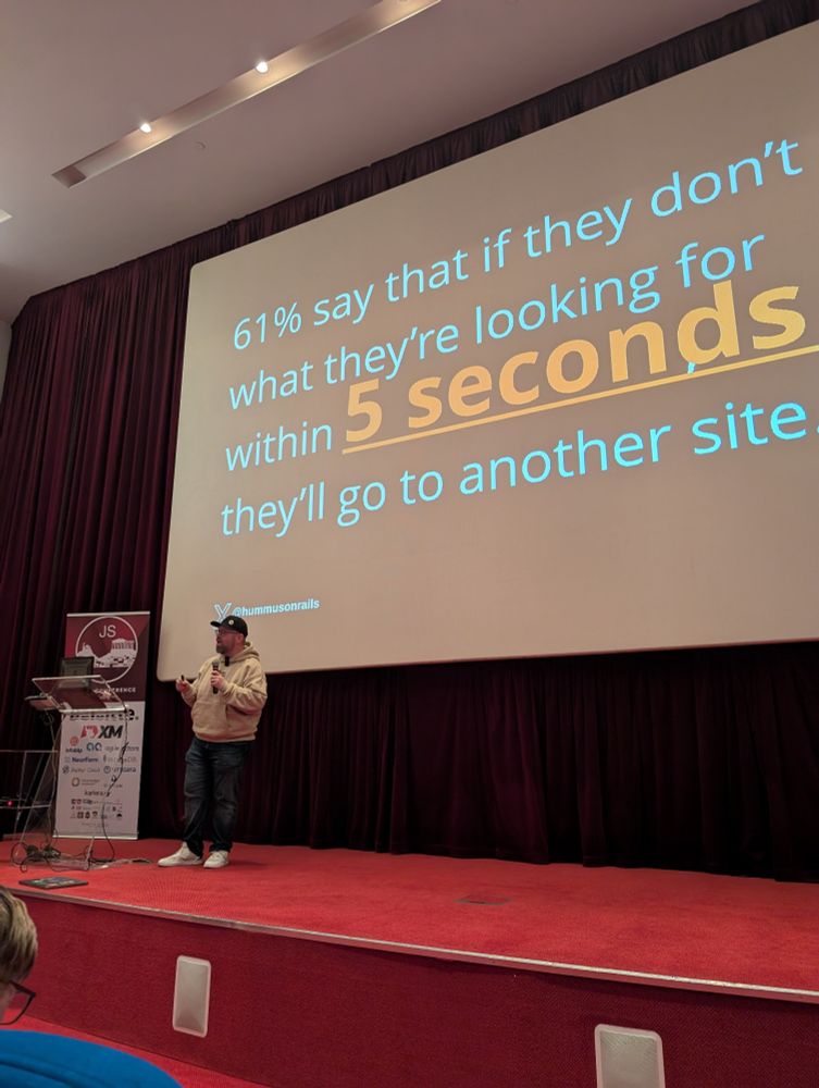 Ben on the left is talking about vector searches on to an auditorium stage with his presentation slides on the back 