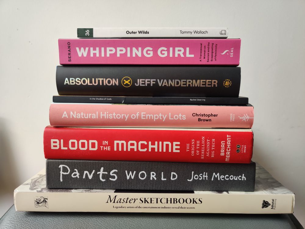A stack of books. 
From top to bottom: 
"Outer Wilds" by Tommy Wallach
"Whipping Girl" by Julia Serano
"Absolution" by Jeff Vandermeer
"In the Shadow of Gods" by Rachel Deering
"A Natural History of Empty Lots" by Christopher Brown
"Blood in the Machine" by Brian Merchant
"Pants World" by Josh Mecouch
"Master Sketchbooks" by 3dTotal Publishing 