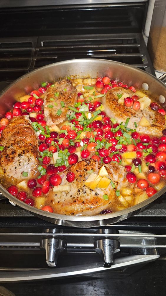 Stainless steel pan on a range top.  Four boneless pork chops in apple and Cranberry light gravy.
