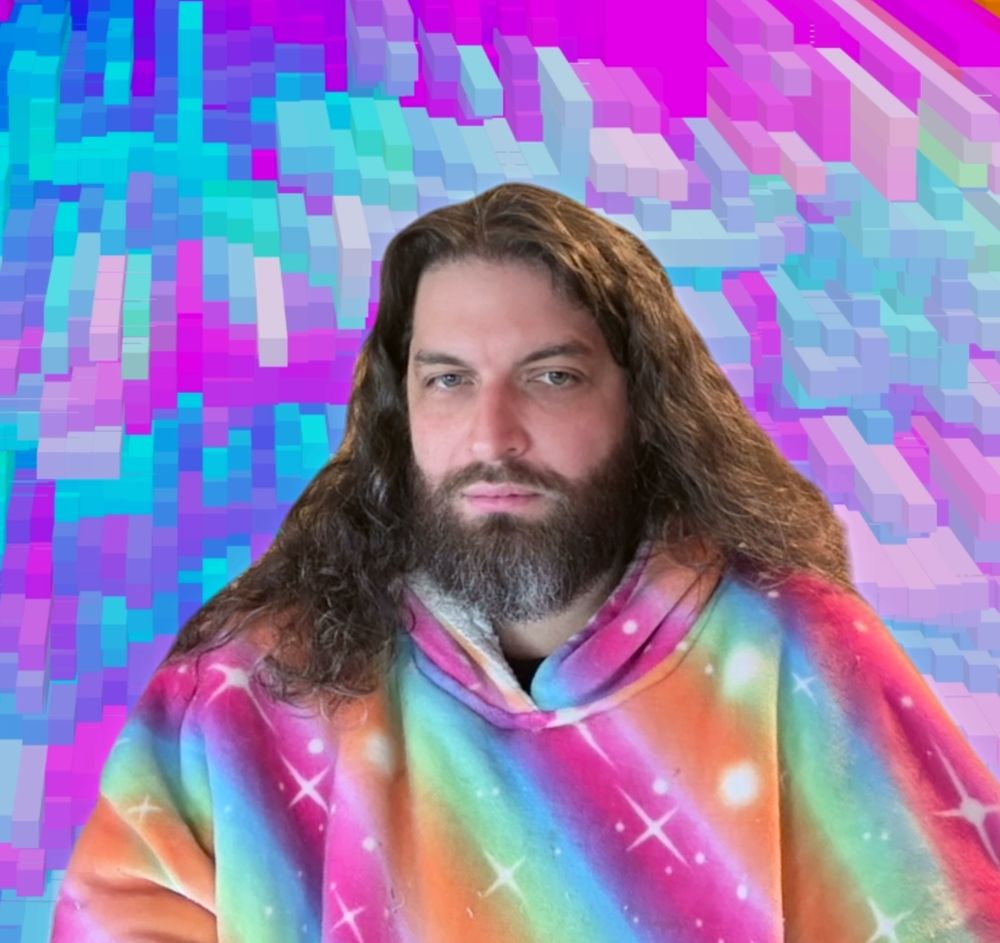 me, a bearded white guy with long wavy hair, in a thick, multicolored space-themed hoodie, set against a zoom background of even more colors arranged in uneven 3d blocks.