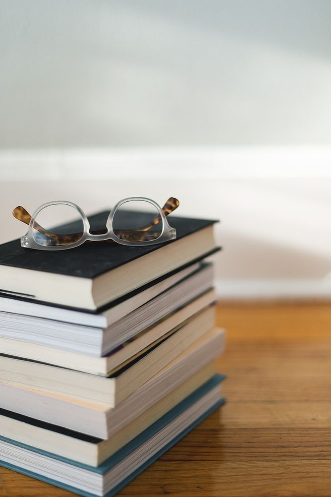 A stack of books on a desk with a pair of glasses resting on top
