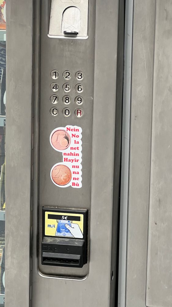 Getränkeautomat mit einem Aufkleber, der 1- und 2-Cent-Münzen zeigt und daneben das Wort Nein in mehreren Sprachen