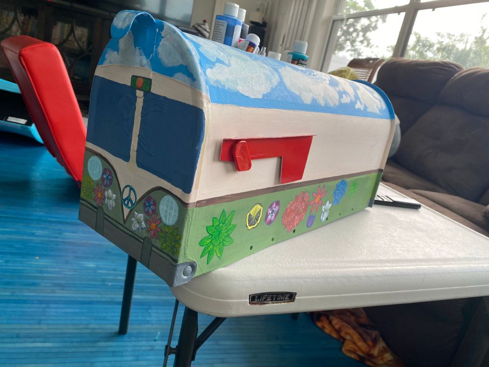 A work in progress of a mailbox painted like a green and tan vw bus with flowers painted on its sides and front