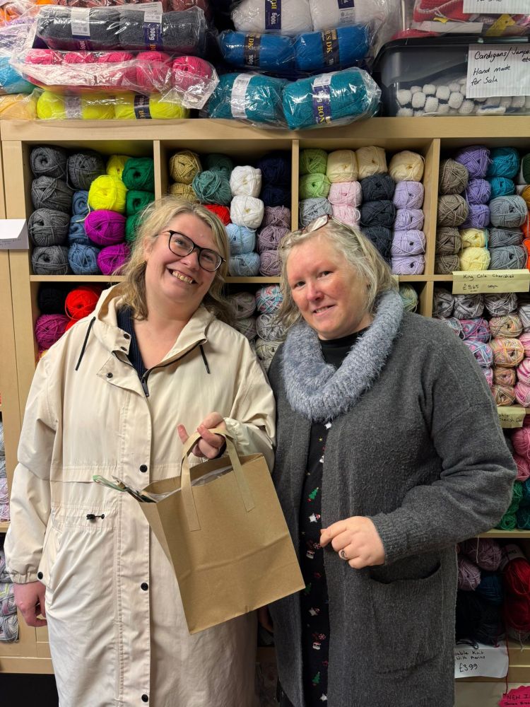 Photo: two women stand in front of hundreds of balls of yarn