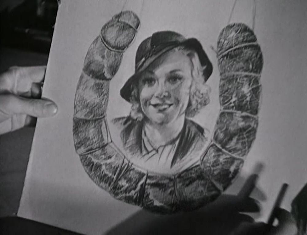 black and white still from Rafter Romance (1933) showing a drawing of Ginger Rogers in a jaunty and stylish cap and jacket, smiling pleasantly, surrounded by a horseshoe of sausage tied up with string, which does in fact look extremely phallic on both ends.