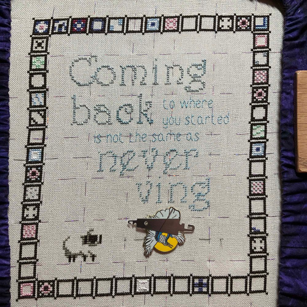 Cross stitch in progress. The brown border boxes are complete but very few of them are filled in even a little bit. The words still say “Coming back to where you started is not the same as never ving”.