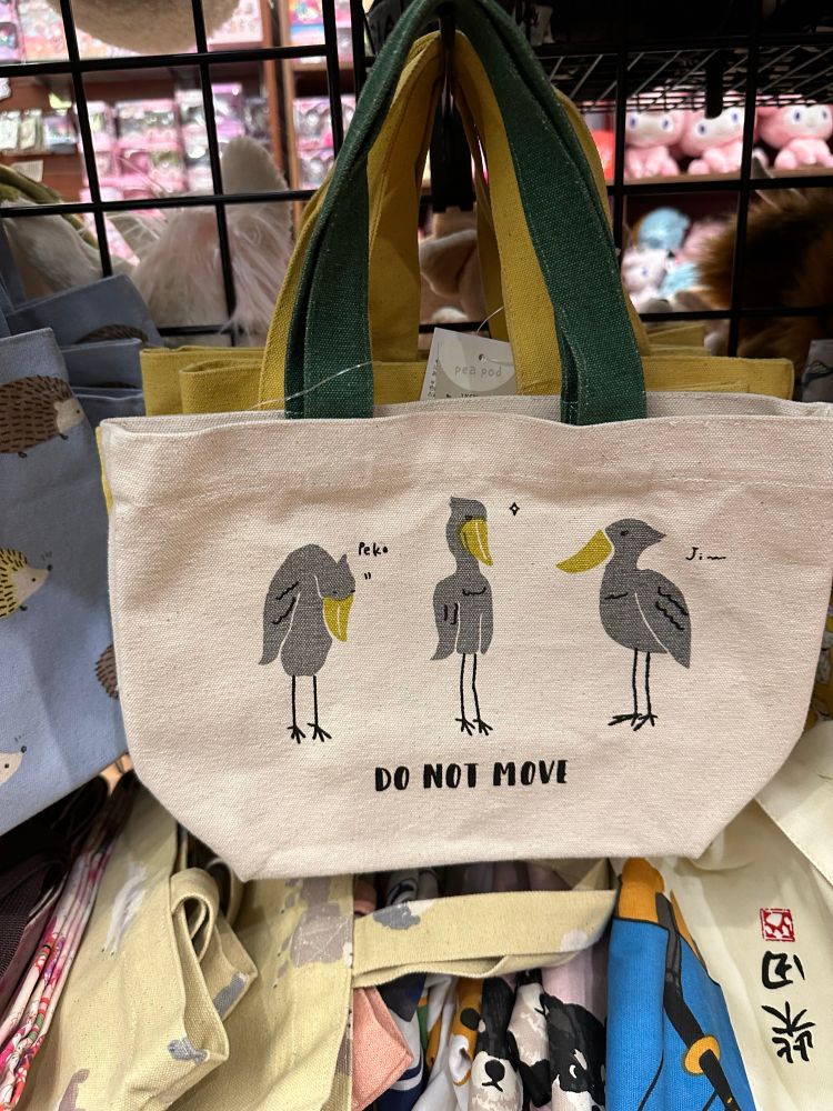 A small white tote bag with green handles that has 3 shoebill birds with the text: DO NOT MOVE under them