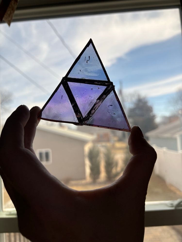 A light purple stained glass triangle being held up to the light