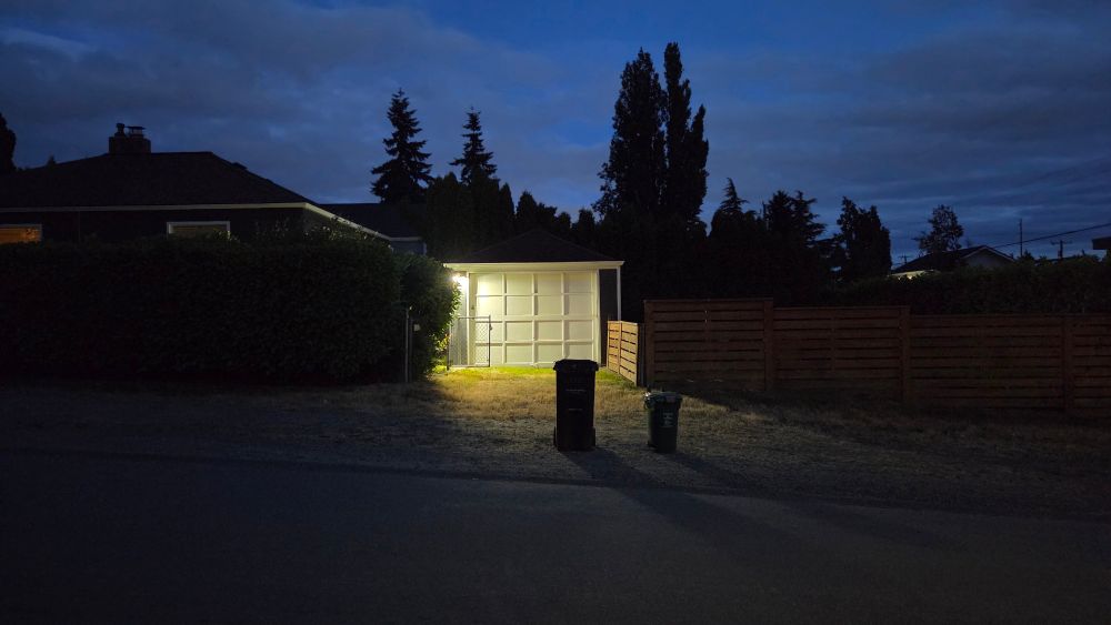 Two garbage bins at the curb after sunset
