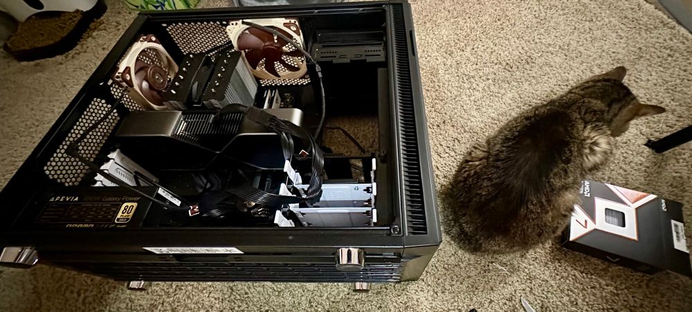 picture of an open PC case lying on carpet. a pet auto feeder and Ryzen 7 CPU box can be seen alongside a cat dutifully guarding the PC case