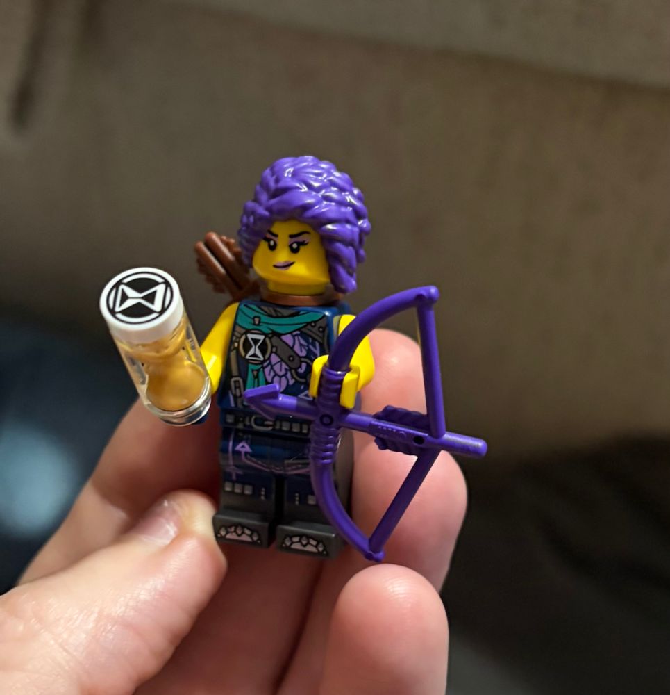 a hella rad Lego figurine with purple hair holding a purple crossbow, a time hourglass, and wearing a SICK looking outfit