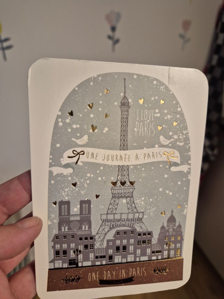 Eine Postkarte aus Paris. Zu sehen ist der Eiffelturm, Schneegestöber und kleine goldene Herzen.