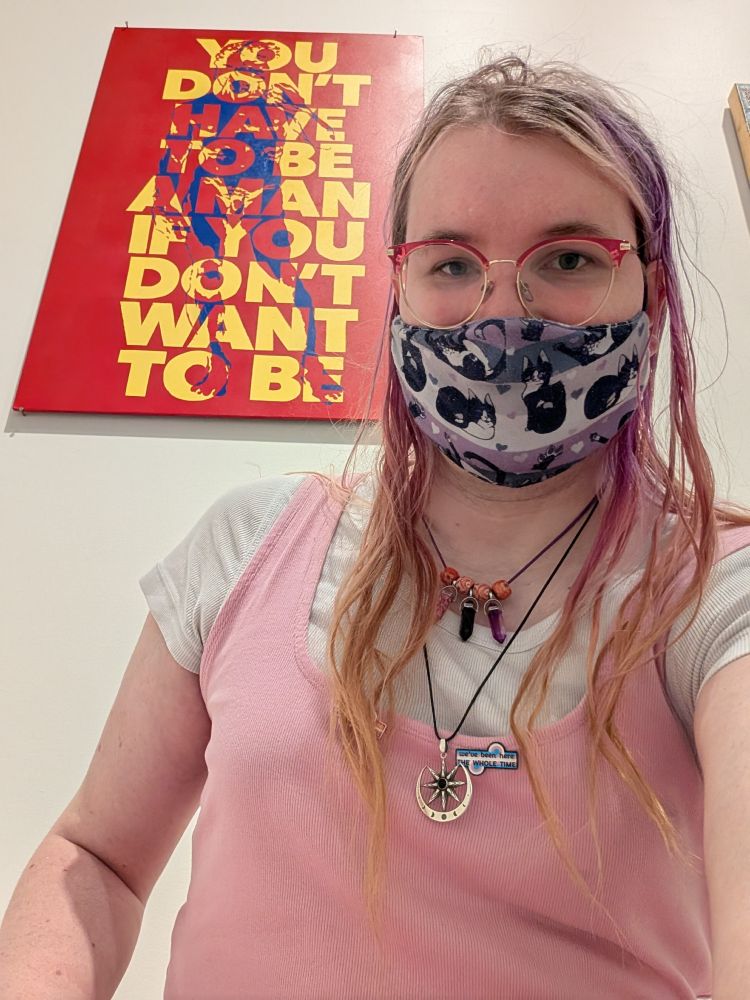 Lower perspective showing an art behind me. The art says YOU DON'T HAVE TO BE A MAN IF YOU DON'T WANT TO BE 